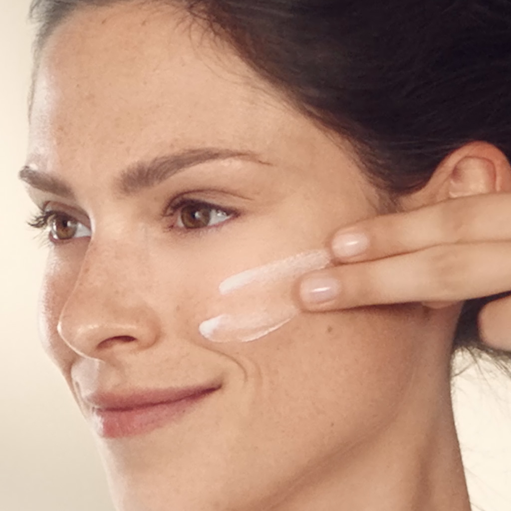 Mujer aplicando protector solar en la mejilla con 